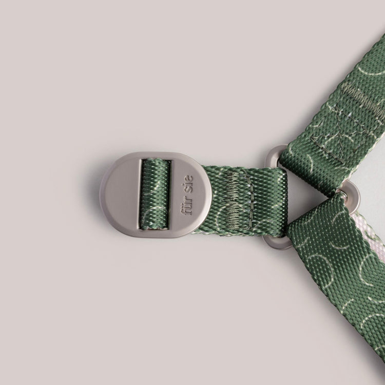Close-up of a Fur Sie Sabine green patterned harness strap with a silver buckle on a light gray background