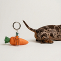 The Snob Fur Sie charm leaning on a carrot dog toy, next to a small dog on a gray background