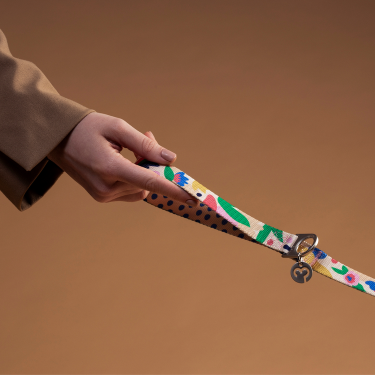 Hand holding the Gaston dog leash with floral and polka dot pattern on a warm neutral background